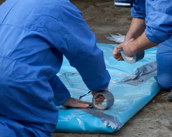 Professional removalists wrapping and sealing asbestos waste in plastic sheets.