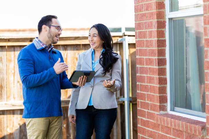 Man and woman outside a brick home looking at a tablet 