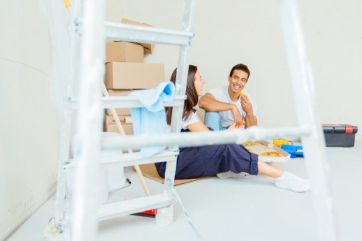 Couple sitting on floor in room with ladder and packing boxes