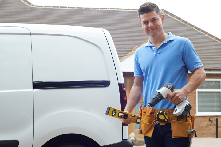 Tradie holding tools standing next to his work van.