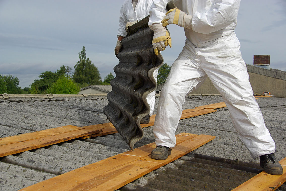 person dressed in white boiler suit removing tiles from a roof.