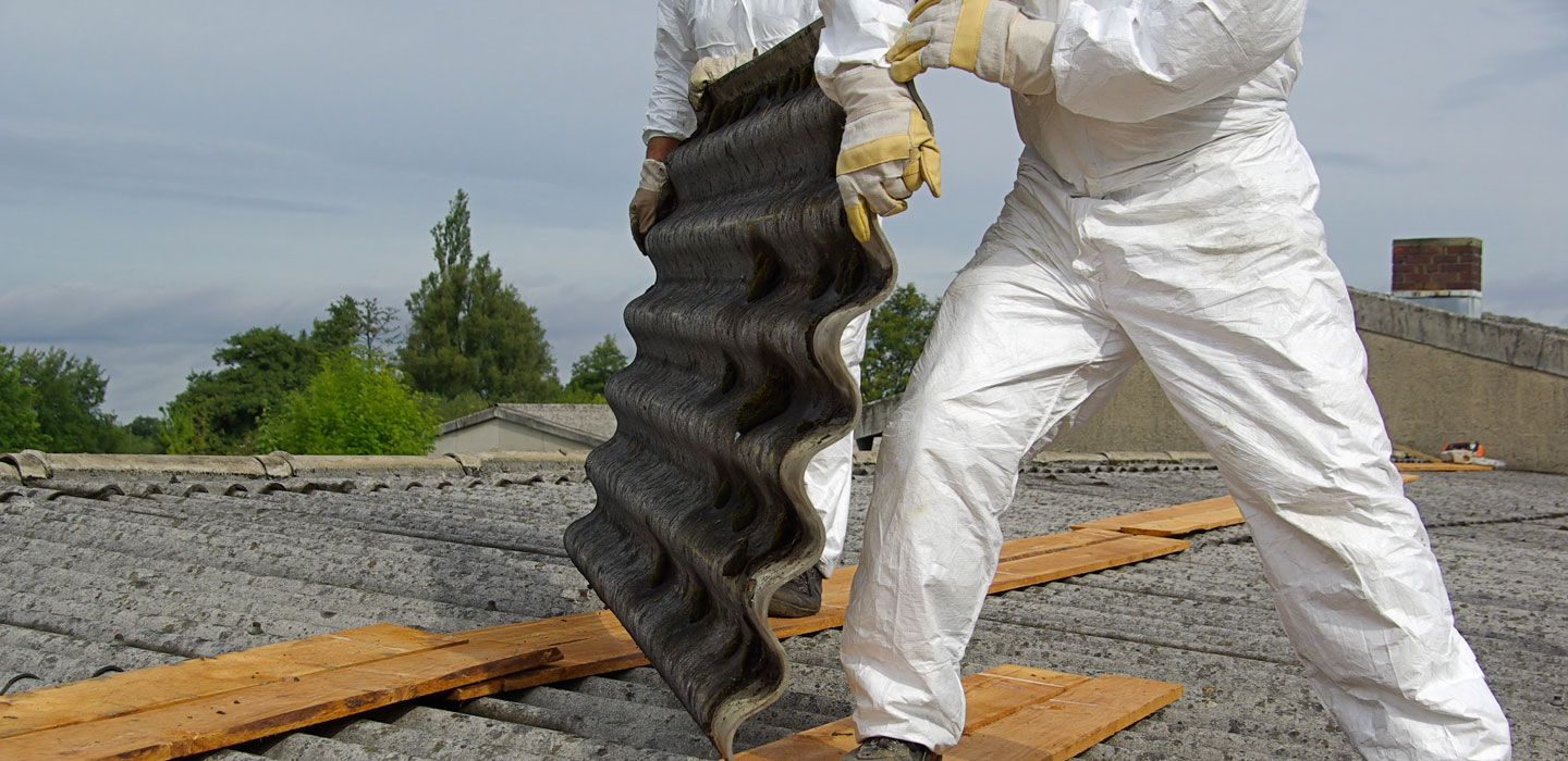 Two people on a roof wearing white boilersuits removing a corrugated roof tile